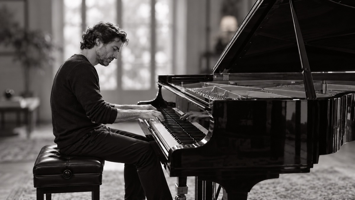 Les mains d’un pianiste sur un piano à queue, nettes devant un arrière-plan flouté, en noir et blanc.